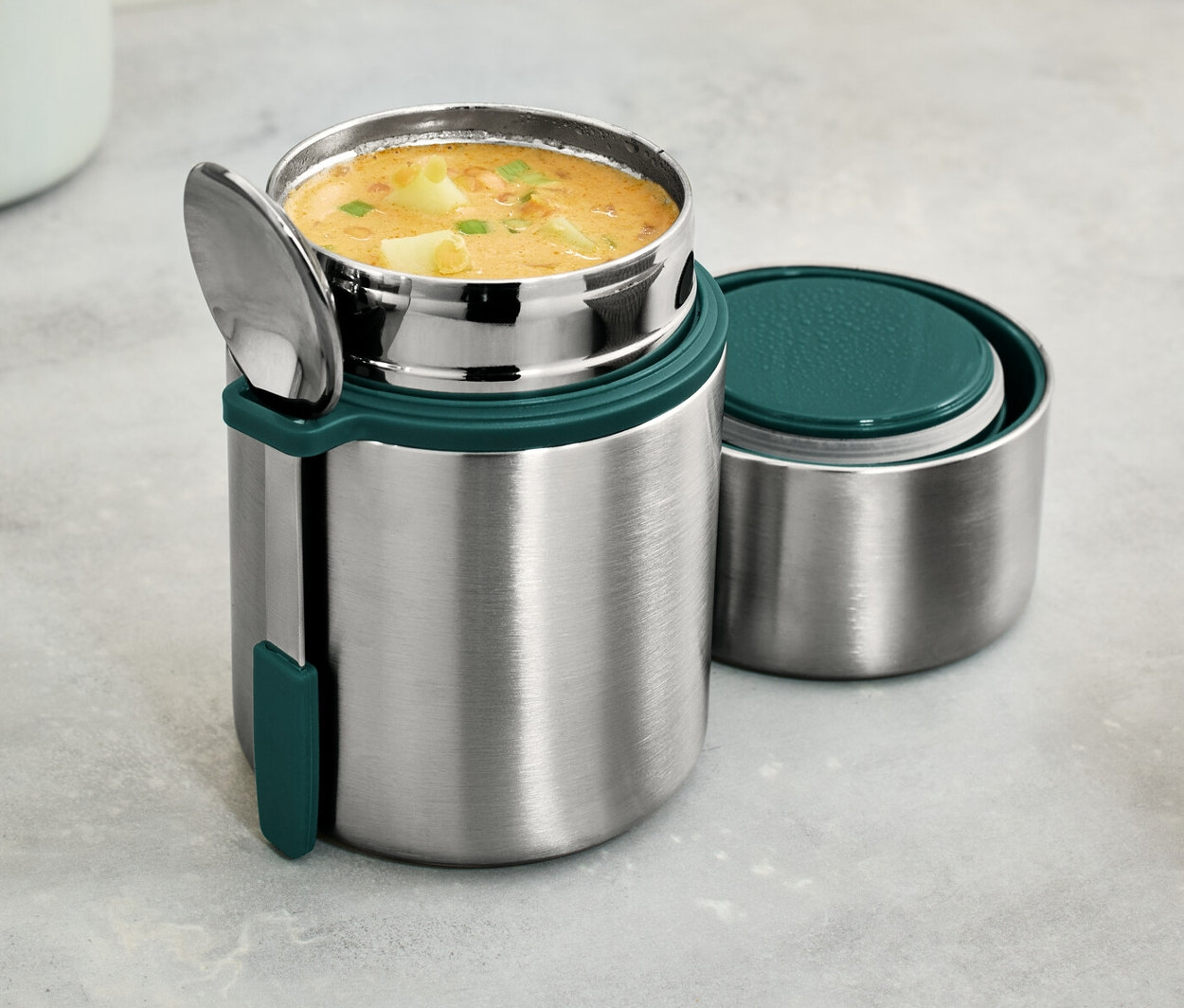 Ein To-go-Thermobehälter aus Edelstahl mit Suppe und Löffel.