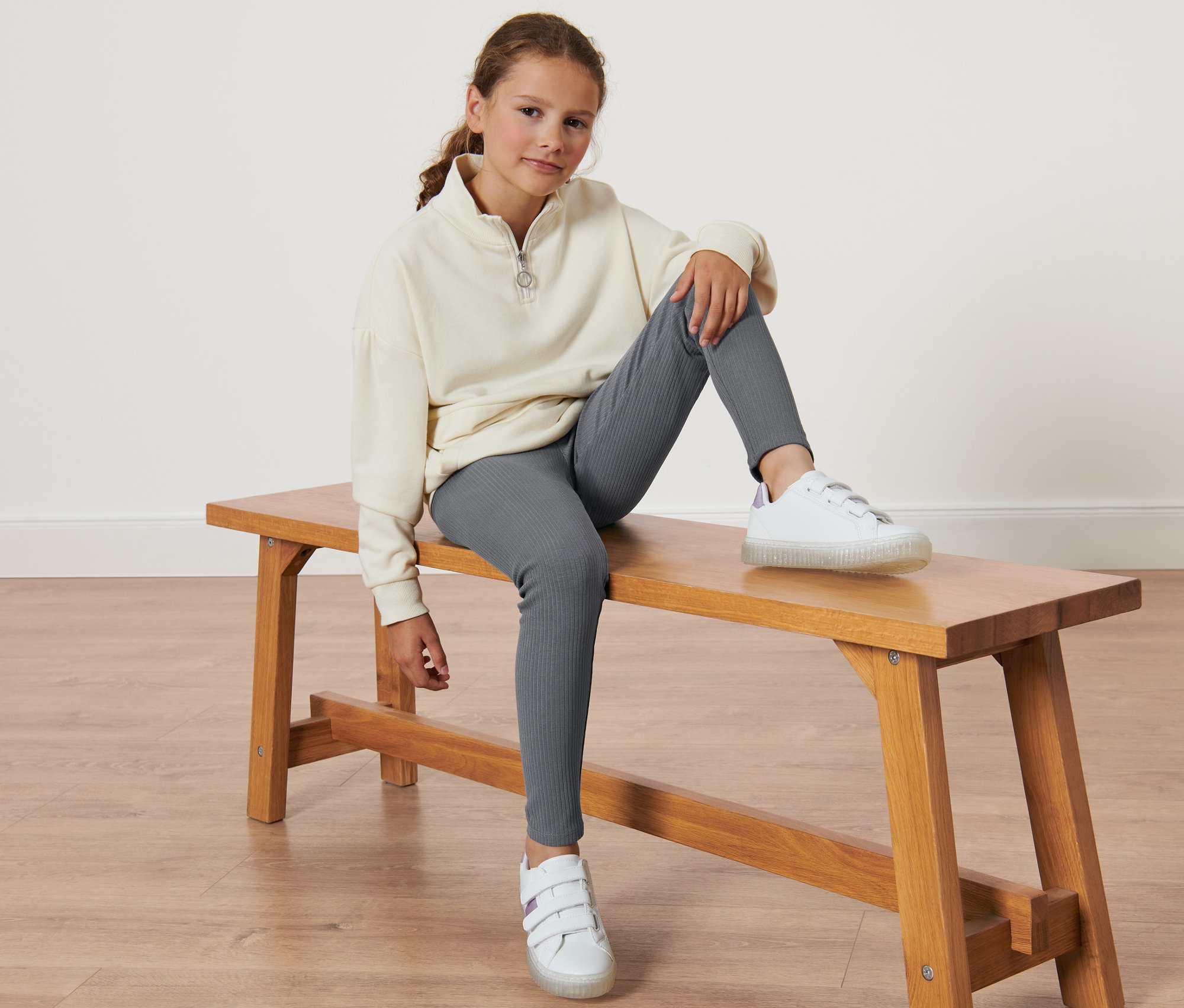 Mädchen sitzt auf einer Bank und trägt eine graue 2 Kinder-Leggings.