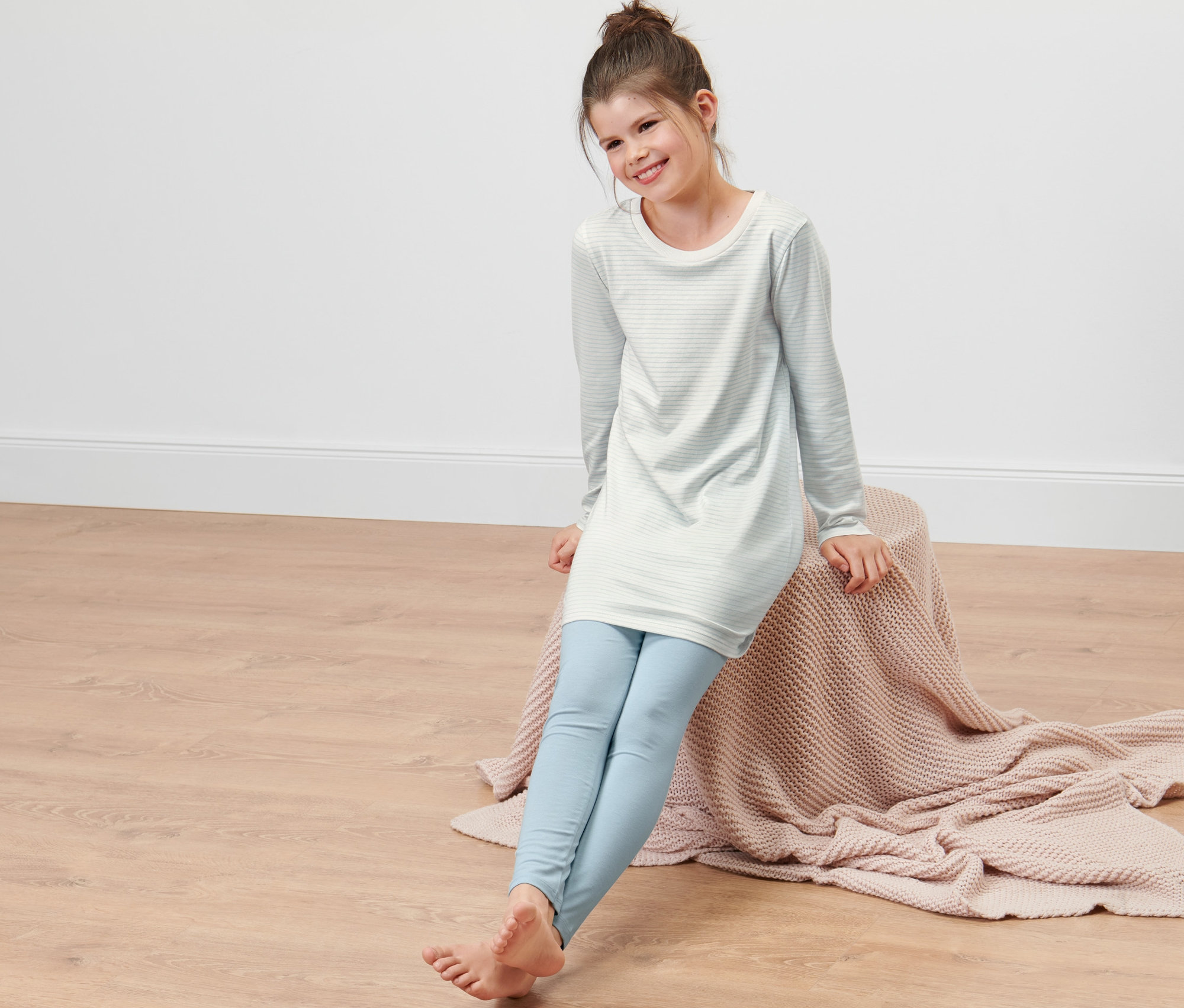 Ein Mädchen sitzt auf einer Decke und trägt einen Kinder-Pyjama.