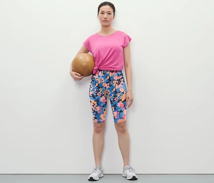 Frau hält Medizinball und trägt Sportradler mit Alloverprint, T-Shirt und Turnschuhe.