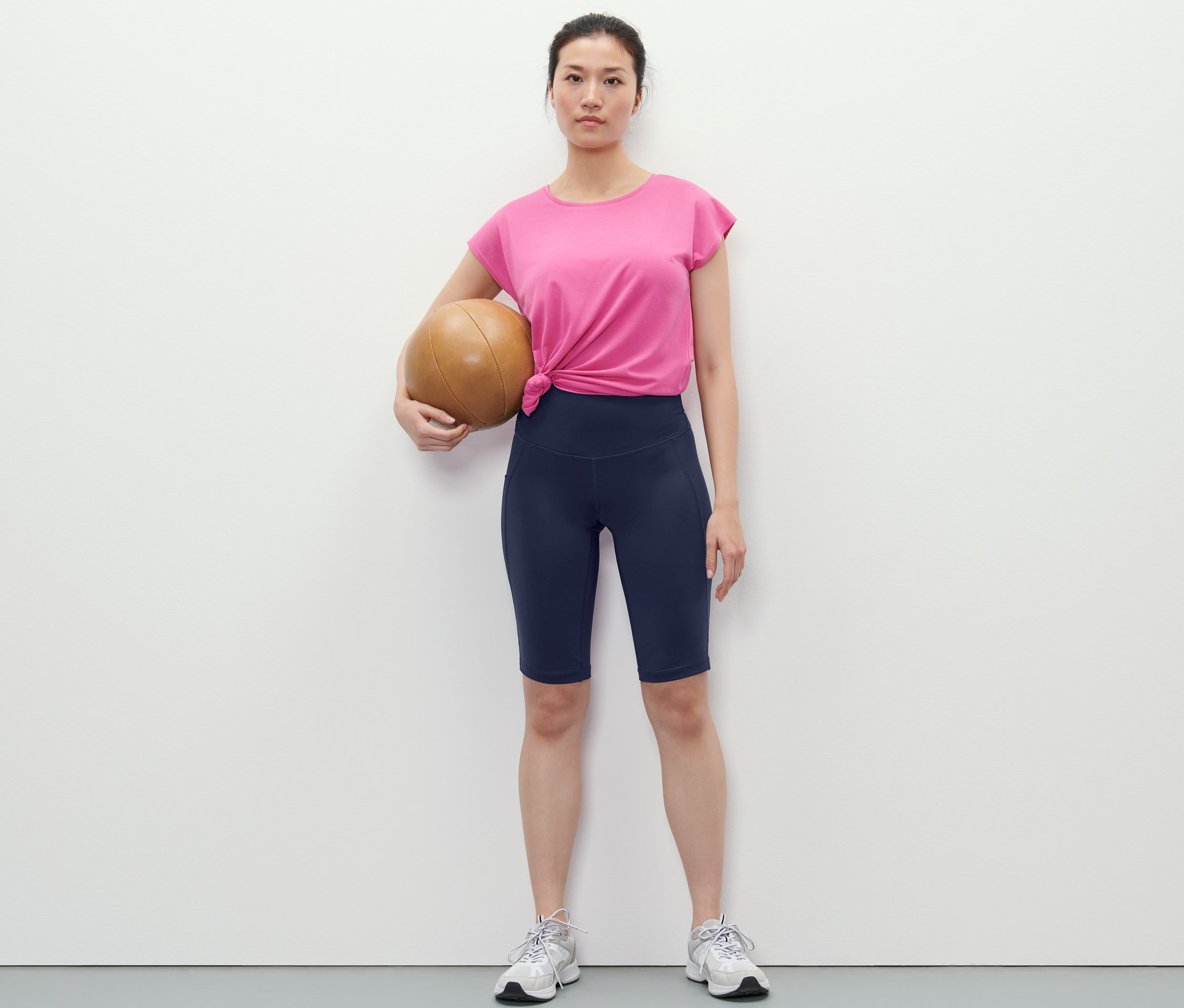 Frau hält einen Basketball und trägt dunkelblaue Sportradler.