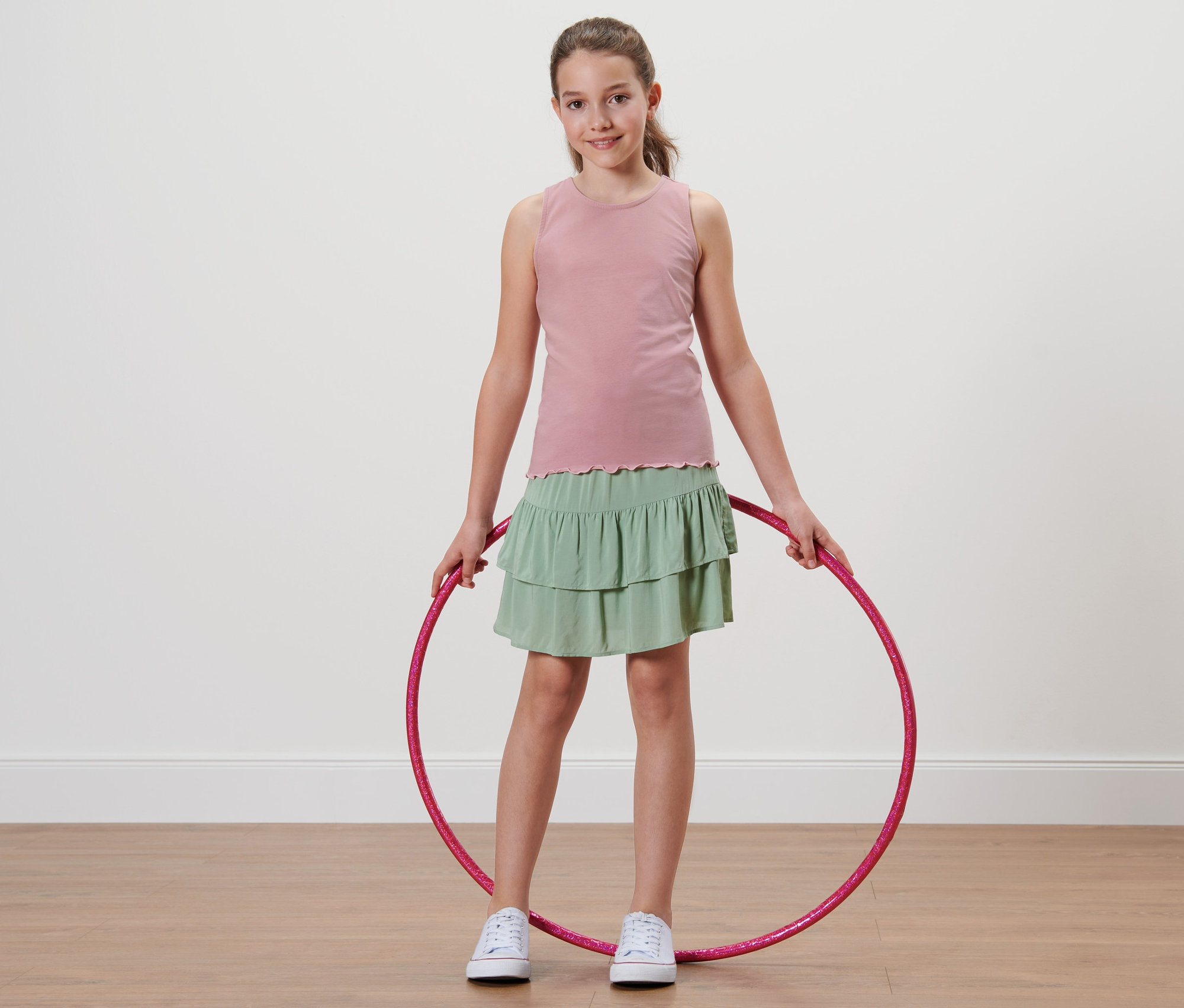 Mädchen hält Hula-Hoop-Reifen und trägt 2 Kinder-Tops.