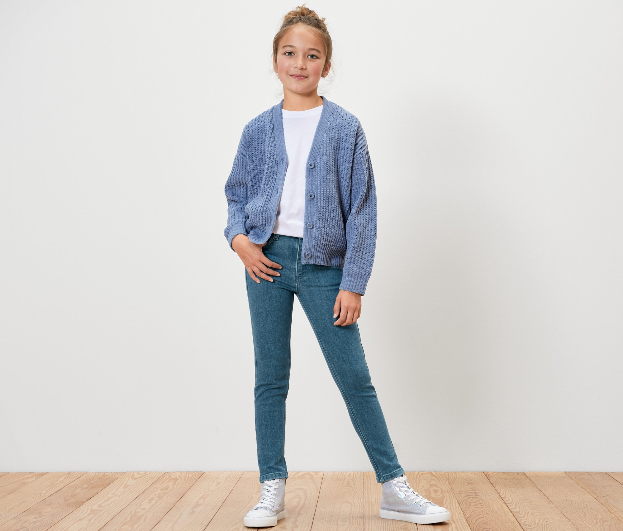 Mädchen posiert stehend in Kinder-Jeans ‒ Fit »Lotta«, weißem T-Shirt und blauer Strickjacke.