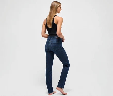 Eine Frau steht mit dem Rücken zum Betrachter und trägt eine dunkelblaue Angels Jeans »Cici« Slim Fit und ein schwarzes Tanktop.