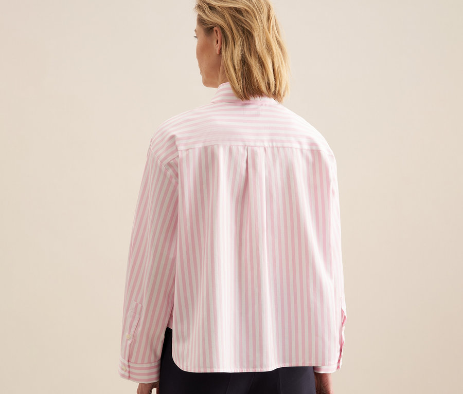 Blonde Frau von hinten, trägt eine roséfarbene, gestreifte Seidensticker Oversize Hemdbluse und eine dunkle Hose.