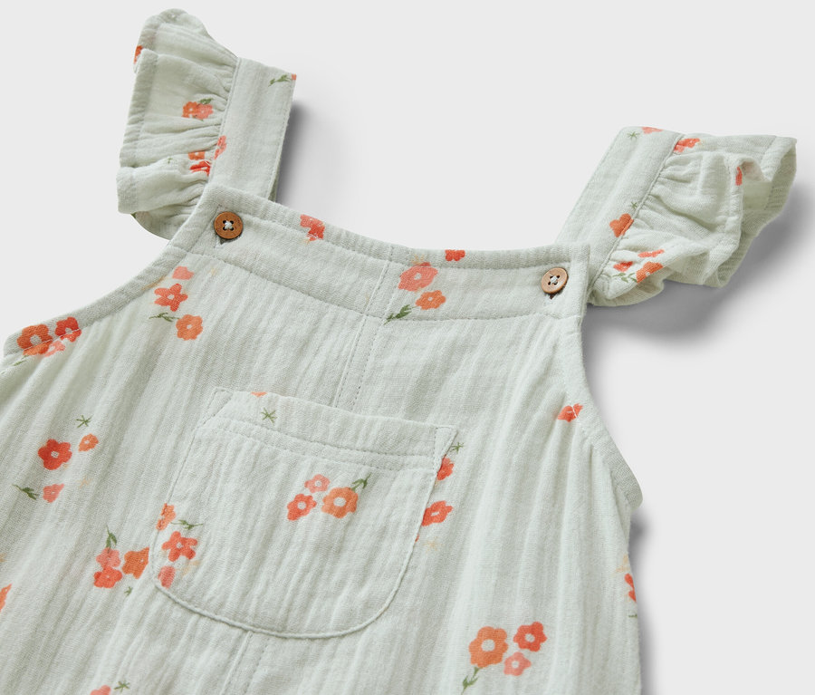 Detailansicht eines Kinder-Musselin-Stramplers mit Blumenmuster und Rüschen an den Trägern.