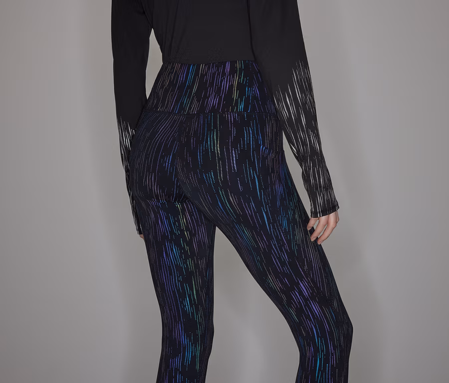 Person trägt ein schwarzes Langarmshirt und glänzende Leggings.