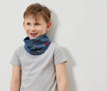 Lächelnder Junge trägt ein blaues Schlauchtuch mit Autoaufdruck und ein graues T-Shirt.