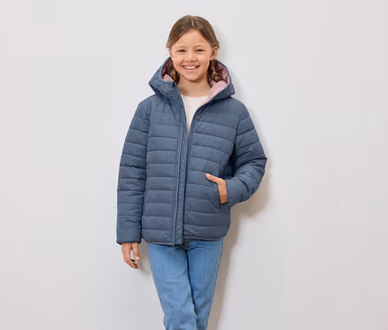 Lächelndes Mädchen trägt eine blaue Steppjacke mit Kapuze und Jeans.