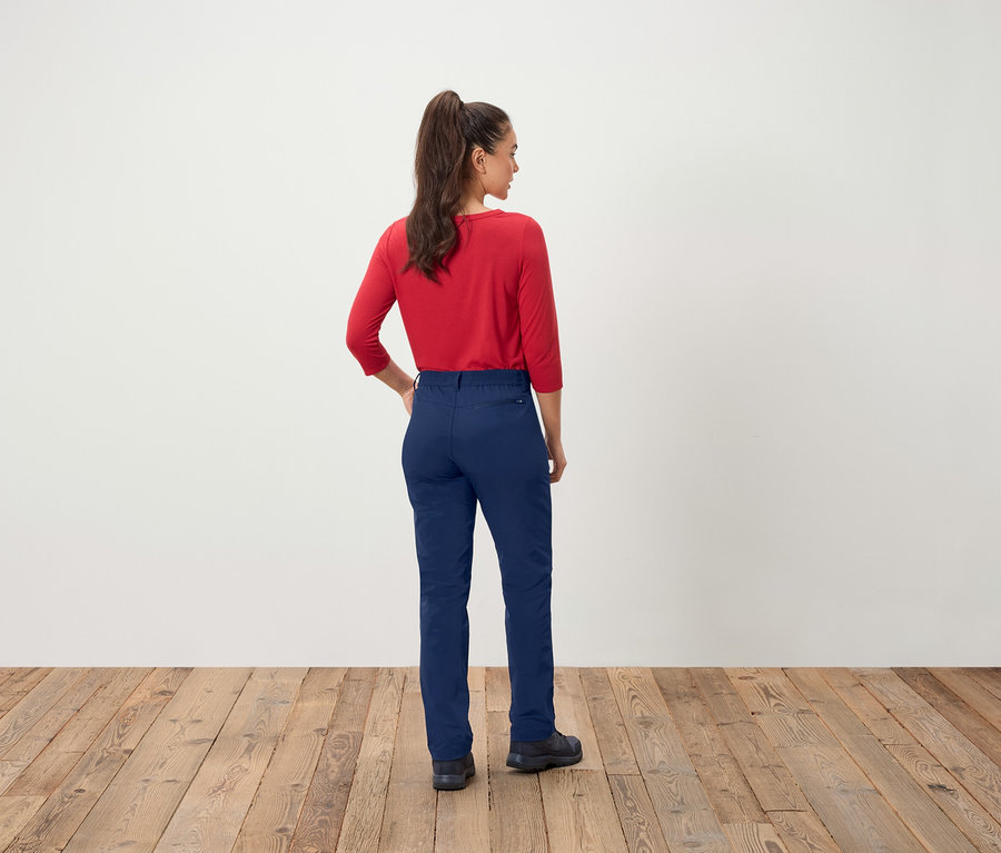 Frau mit rotem Oberteil und blauen Hosen steht mit dem Rücken zur Kamera.