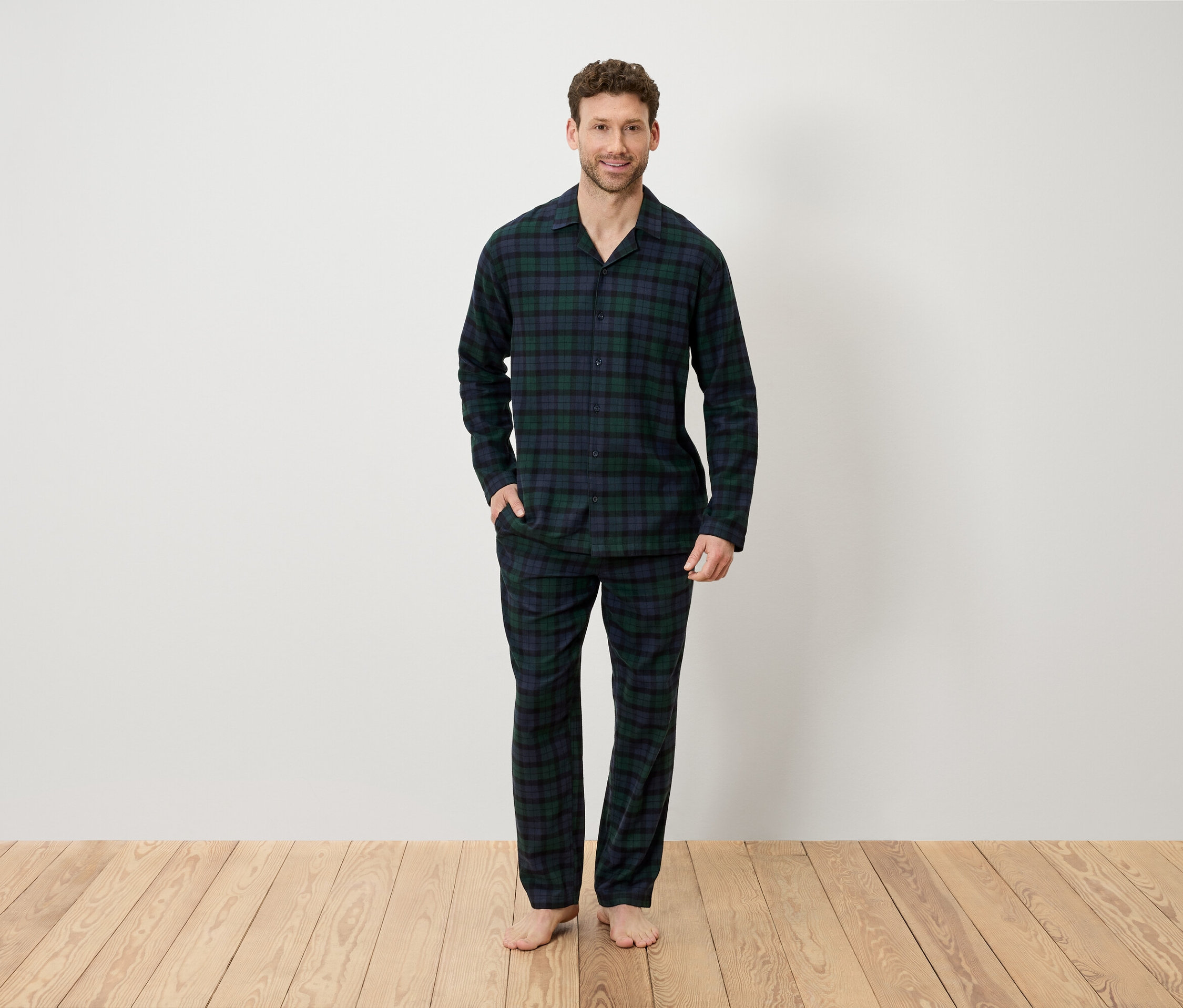 Mann im karierten Pyjama steht auf einem Holzboden vor einer weißen Wand.