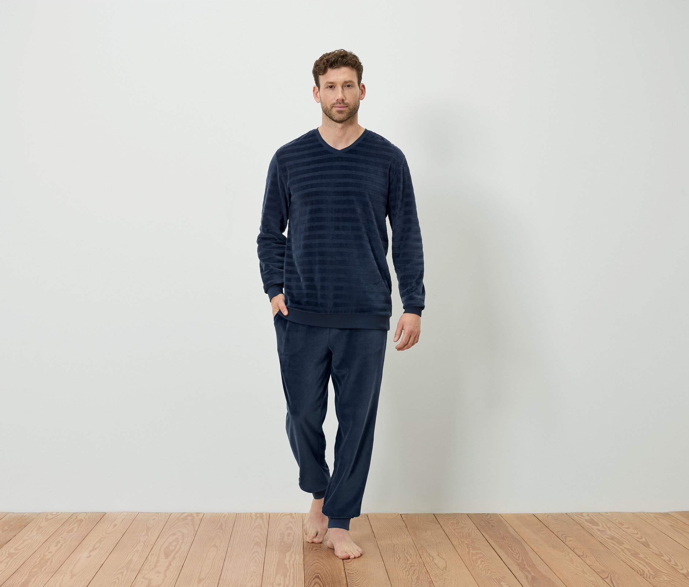Mann steht barfuß und trägt einen dunkelblauen, gestreiften Schlafanzug.