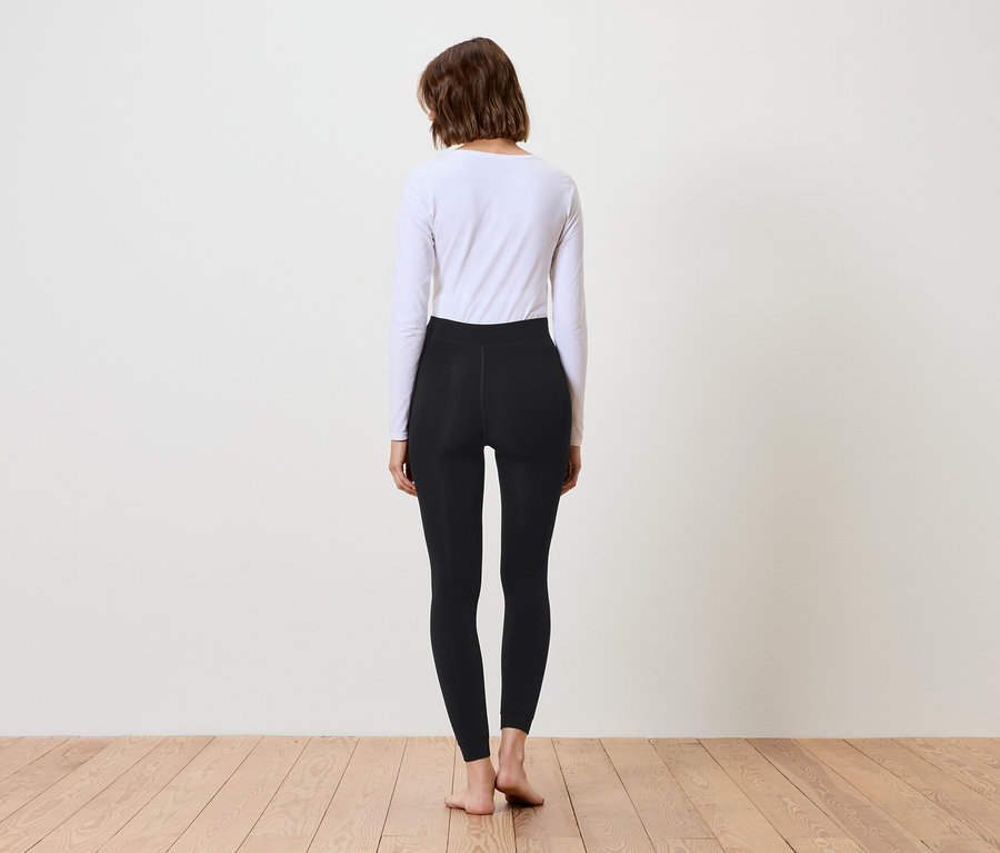 Frau von hinten trägt schwarze Leggings und ein weißes Langarmshirt.