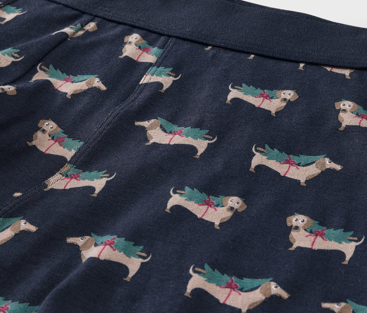Detailansicht von blauen Boxershorts mit Dackel-Print, die Weihnachtsbäume tragen.