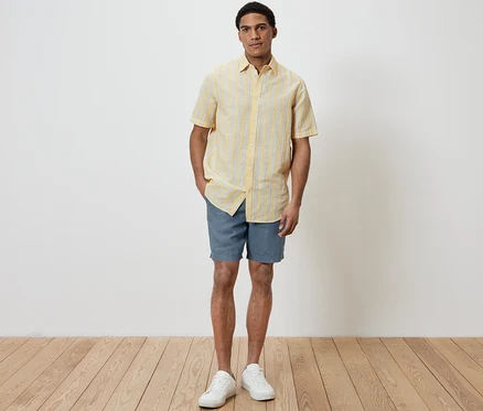 Mann steht und trägt ein gelbes Kurzarmhemd mit Leinen und blaue Shorts.