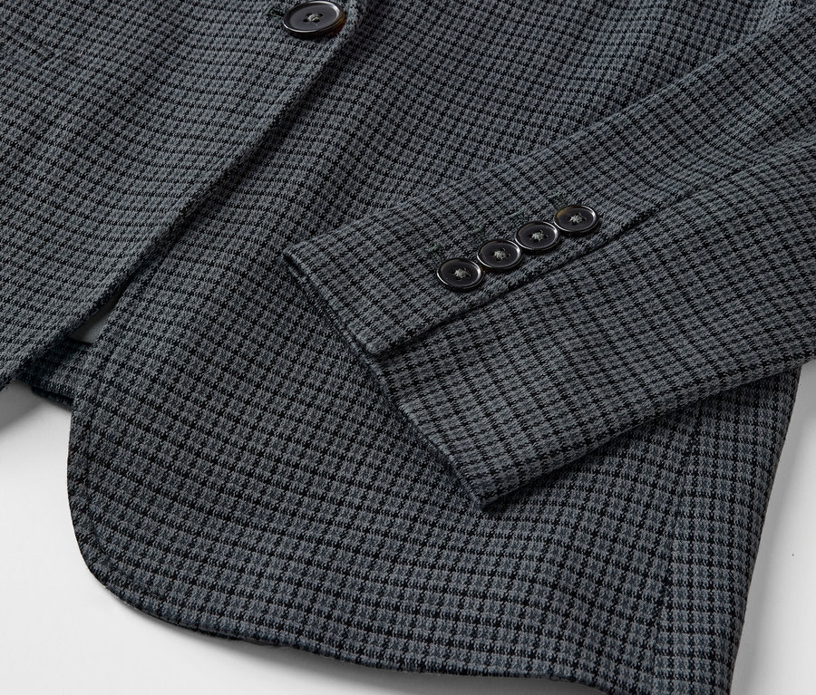 Detailaufnahme eines grauen Blazers mit kleinem Muster und Knöpfen am Ärmel.