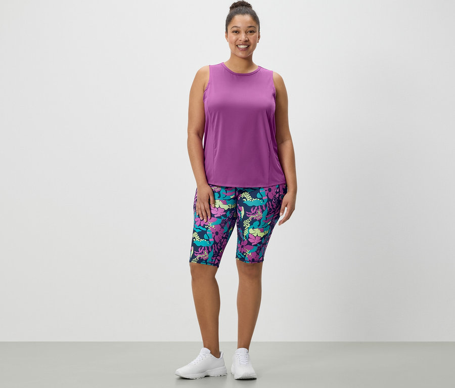 Eine Frau steht und trägt Sportradler mit Alloverprint und ein türkises Sport-Top aus einem 2er-Set.