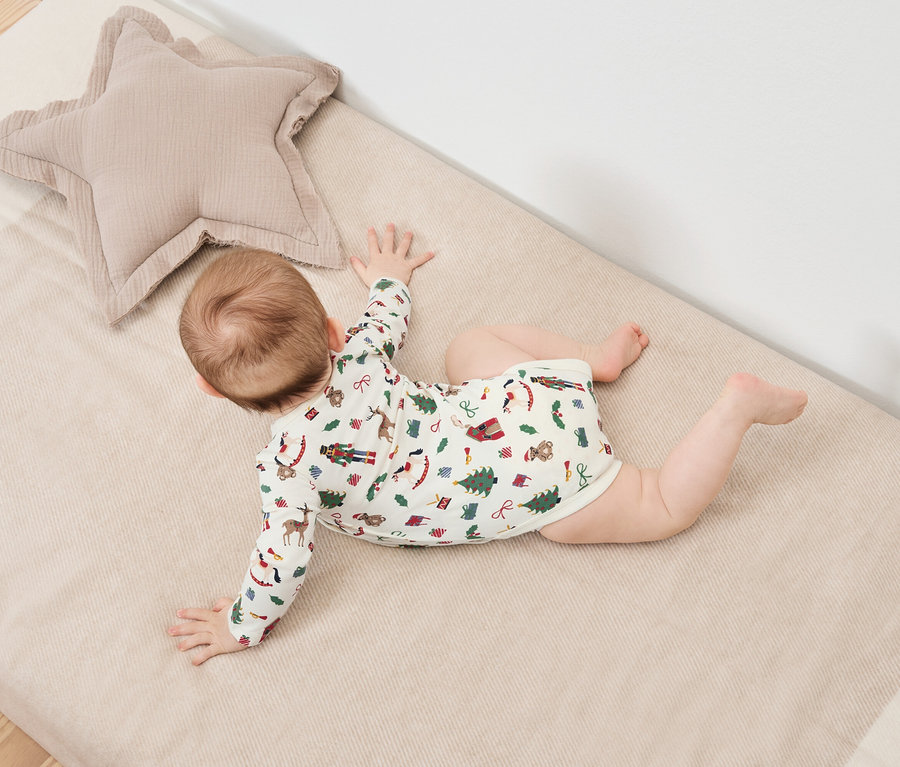 Baby liegt auf dem Bauch auf einer Decke mit Weihnachtsmotiven neben einem beigen sternförmigen Kissen.