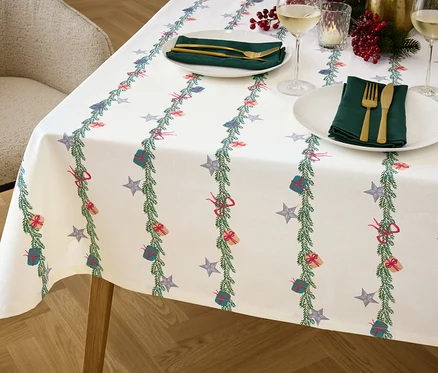Detailaufnahme eines Tisches mit einer weihnachtlichen Tischdecke, Tellern, Besteck und Gläsern.