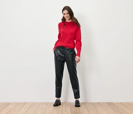 Frau posiert in rotem Pullover und schwarzen Lederhosen.