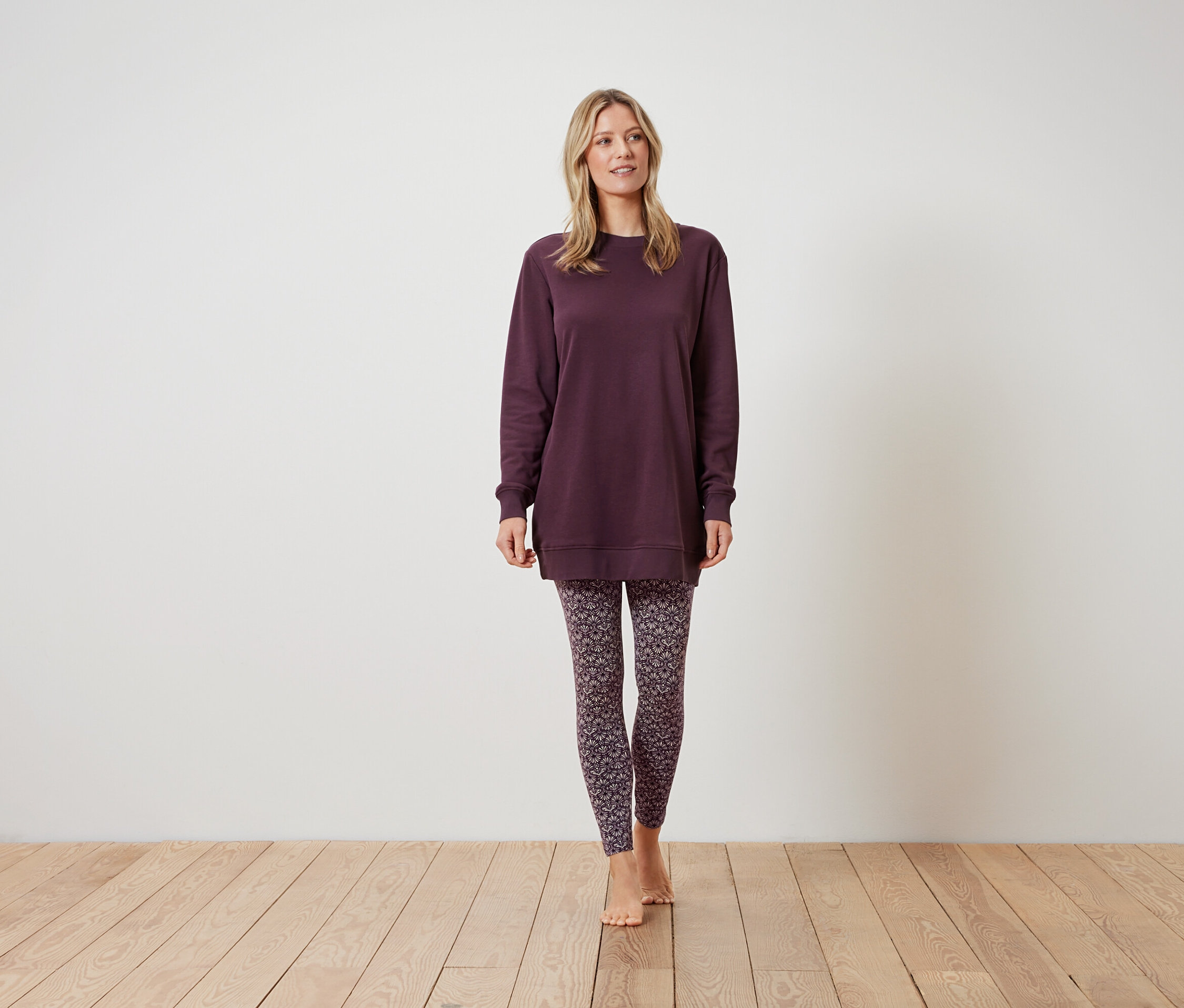 Frau steht und trägt ein weinrotes Sweatshirt und gemusterte Leggings.