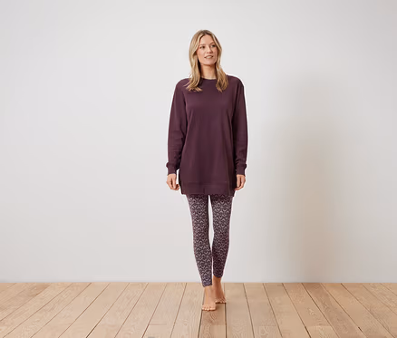 Frau steht und trägt ein weinrotes Sweatshirt und gemusterte Leggings.