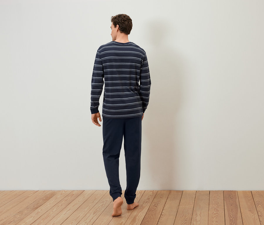 Mann im gestreiften Schlafanzug geht barfuß über Holzboden.