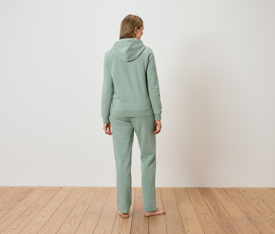 Rückansicht einer Frau mit langen blonden Haaren, die einen hellgrünen Hoodie und eine passende Hose trägt.