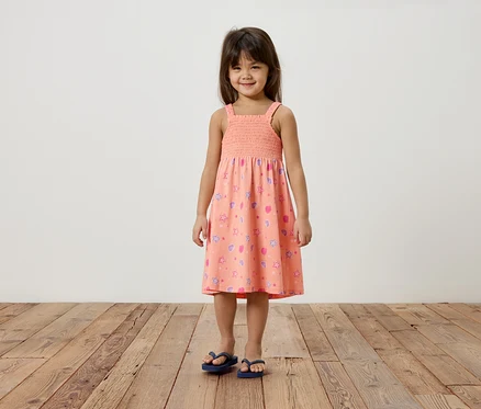 Mädchen mit braunen Haaren trägt ein rosa Sommerkleid mit Sternen und Herzchen und blaue Flip-Flops.