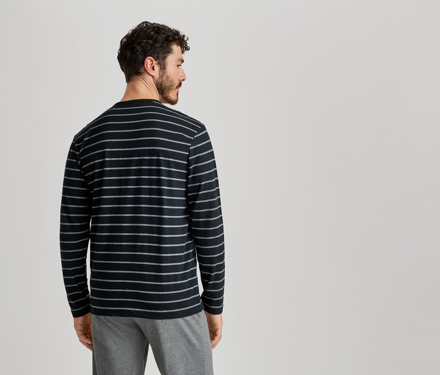 Mann von hinten, trägt ein schwarz-gestreiftes Langarmshirt und graue Hose vor einem hellen Hintergrund.