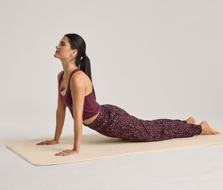 Frau in Sportbekleidung macht Yoga auf einer beigen Matte, in Kobra-Pose.