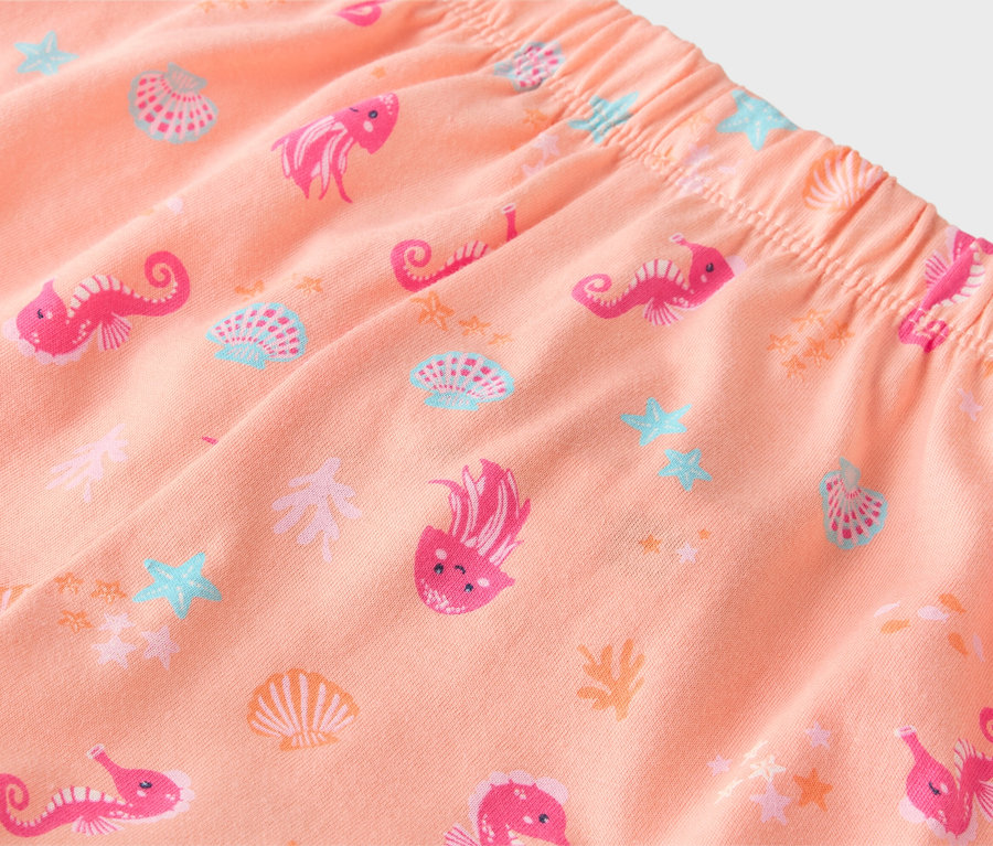 Nahaufnahme einer Pfirsich-farbenen Hose mit elastischem Bund, bedruckt mit rosa Seepferdchen, Quallen und Muscheln.