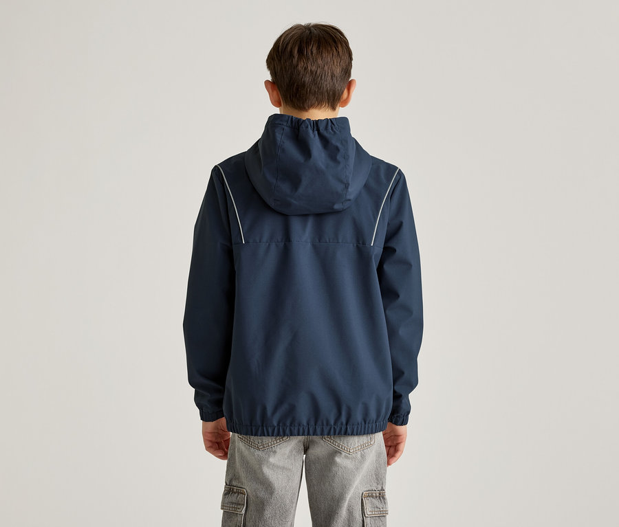 Rückansicht eines Jungen mit marineblauer Kapuzenjacke mit weißen Streifen und grauer Cargohose vor einem hellen Hintergrund.