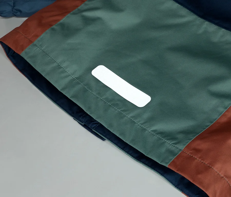 Nahaufnahme einer Jacke mit marineblauen, grünen und braunen Farbblöcken und einem reflektierenden Detail.