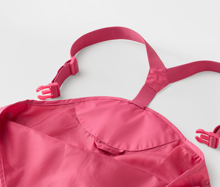 Nahaufnahme einer pinkfarbenen Kinder-Regenhose mit verstellbaren Hosenträgern und Schnallen auf einem weißen Hintergrund.
