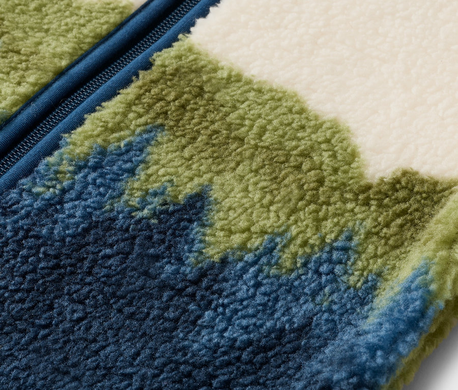 Nahaufnahme einer Fleecejacke mit blauem Reißverschluss und einem Muster aus blauen, grünen und weißen Farbtönen.