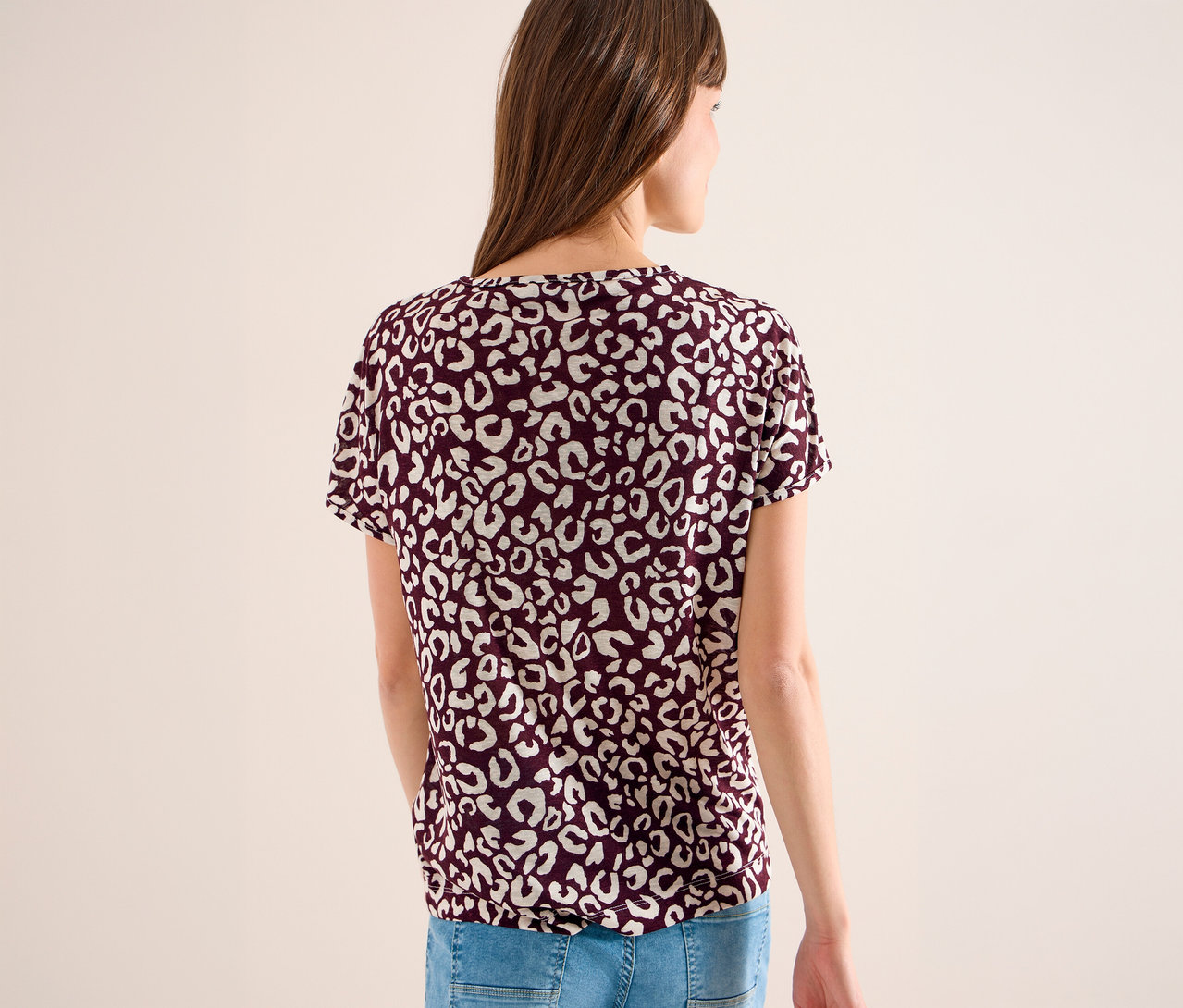 Frau von hinten in bordeauxrotem T-Shirt mit weißem Leopardenmuster und blauen Jeans.