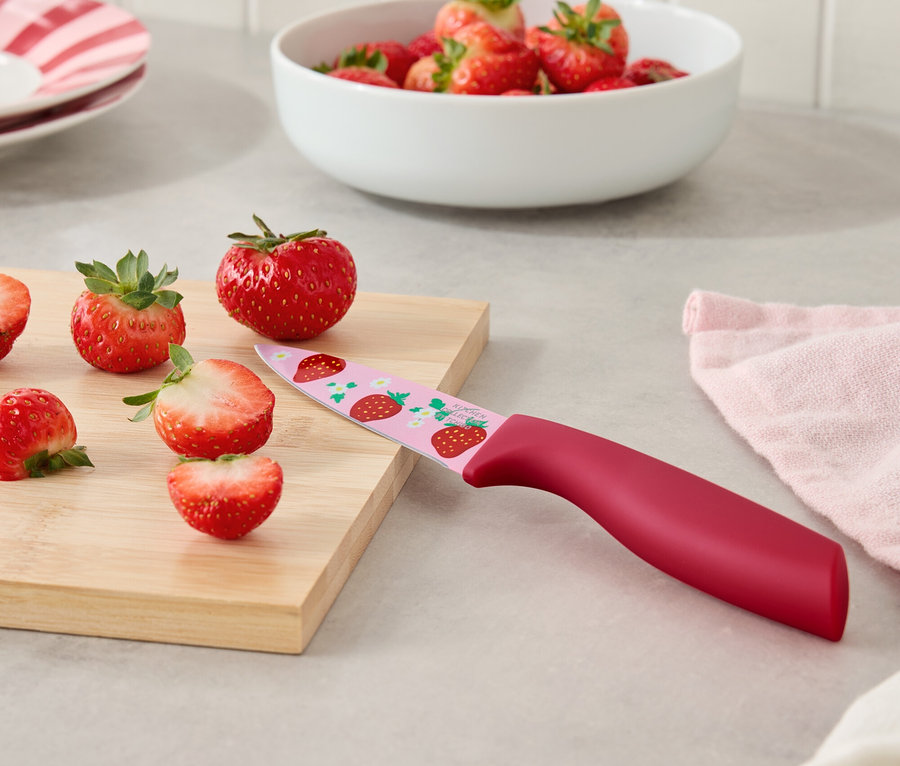 Erdbeeren und ein Messer mit Erdbeermuster auf einem Schneidebrett.