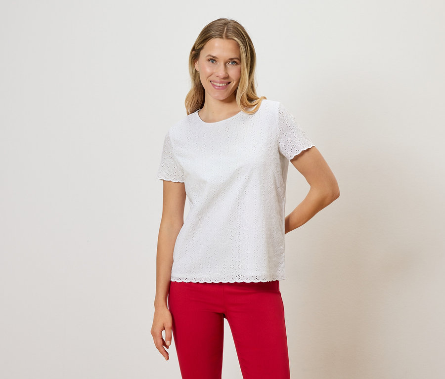 Frau mit blonden Haaren trägt ein weißes Lochstickerei-T-Shirt und eine rote Hose.