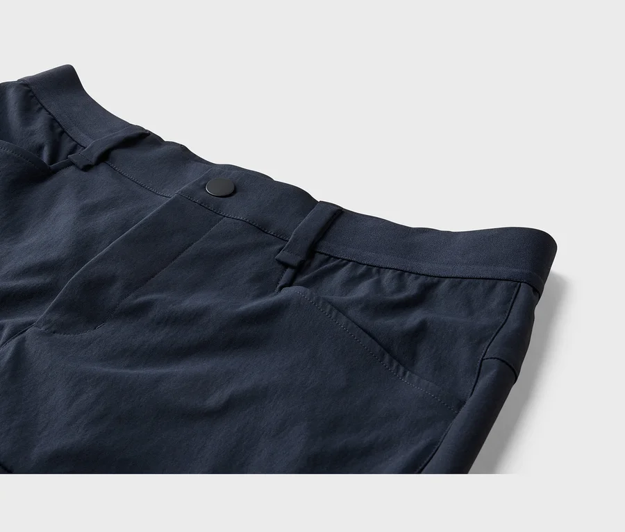 Dunkelblaue Hose, Nahaufnahme des Hosenbunds mit schwarzem Knopf, Gürtelschlaufen und Vordertasche.