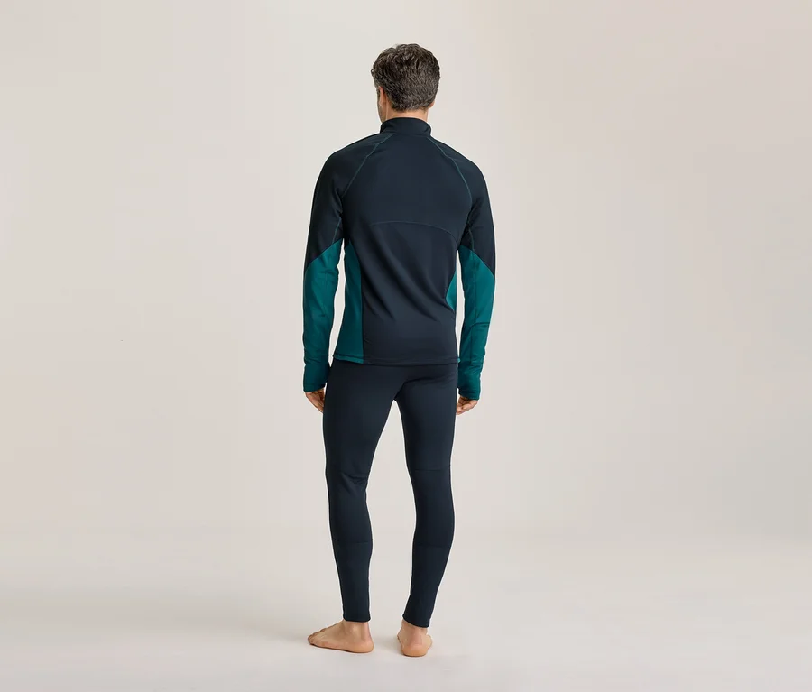 Mann von hinten, trägt ein dunkelblaues und türkises Langarmshirt und dunkelblaue Leggings, barfuß stehend.