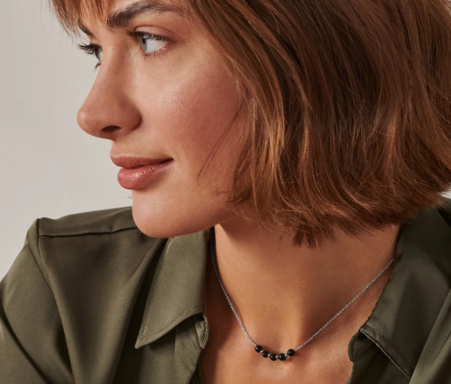 Profil einer Frau mit braunen Haaren und einem grünen Hemd, die eine Energie-Obsidian-Kette trägt.