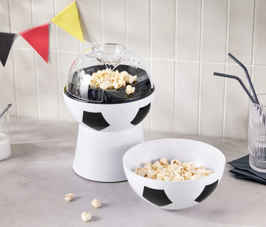 Ein Popcorn-Maker in Fußballoptik steht neben einer Schüssel Popcorn und einem Glas mit Strohhalmen.
