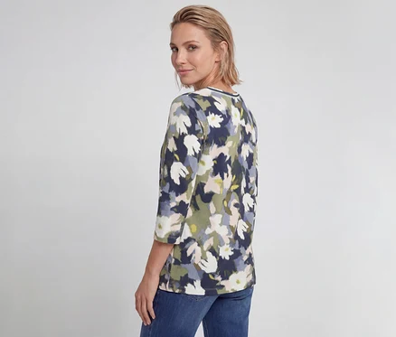 Frau trägt ein Olsen 3/4-Shirt mit marineblauem, grünem und weißem Blumenmuster und blickt über die Schulter.