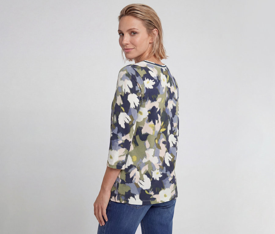 Frau trägt ein Olsen 3/4-Shirt mit marineblauem, grünem und weißem Blumenmuster und blickt über die Schulter.