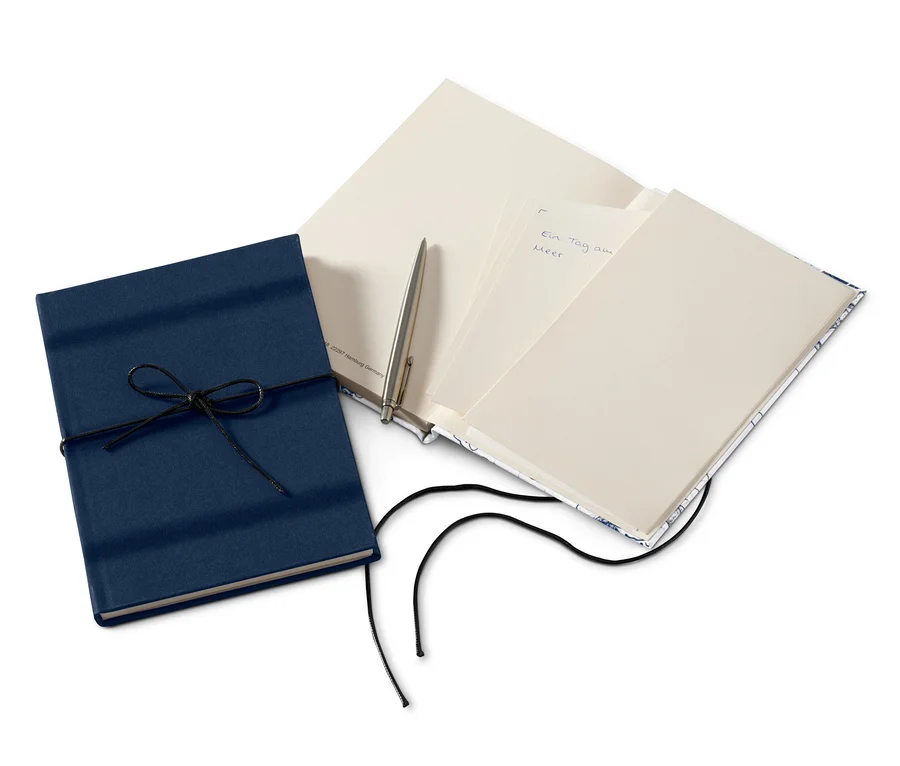 Zwei Notizbücher, eines blau mit Kordel, das andere offen mit Stift.