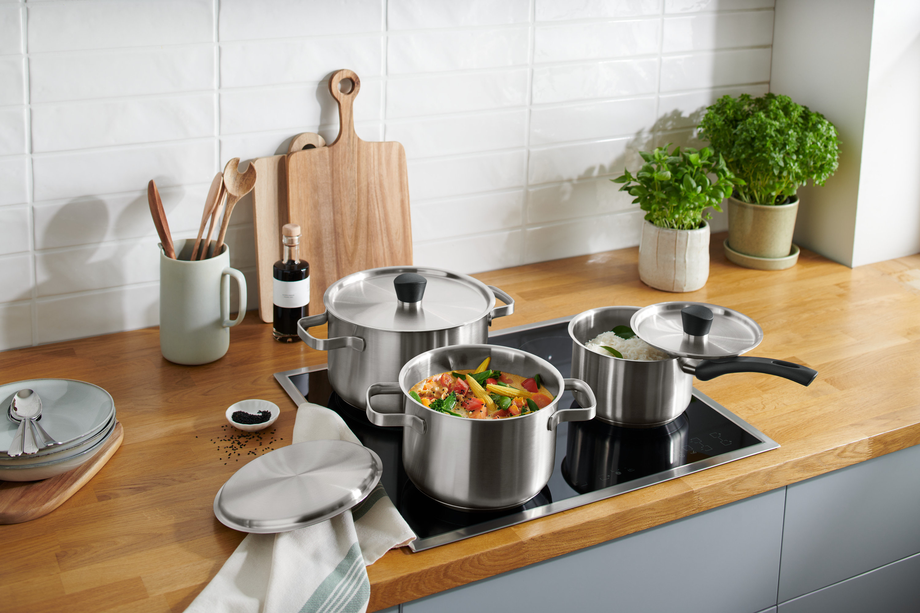 Edelstahl-Kochtopf-Set steht auf einem Induktionskochfeld, eines mit Gemüse, eines mit Reis.