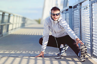 Sportjacken für alle Situationen: Ein junger Mann in einer weissen Laufjacke macht mit Kopfhörern Stretch-Übungen auf einer Brücke.