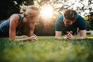 Ein Mann und eine Frau machen ohne Outdoor Fitnessgeräte Sport im Park und haben Spass dabei.