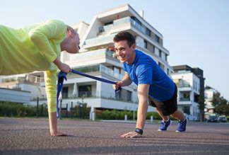 Einfaches Fitnessgerät: Ein junges Pärchen macht gemeinsam eine Übung mit einem Thera-Band auf einer ruhigen Strasse in urbaner Umgebung.